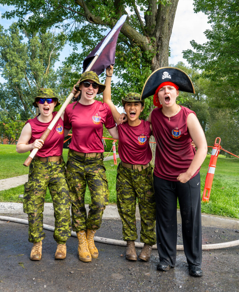 Four people in uniform cheering, one holding a flag and another wearing a pirate hat.