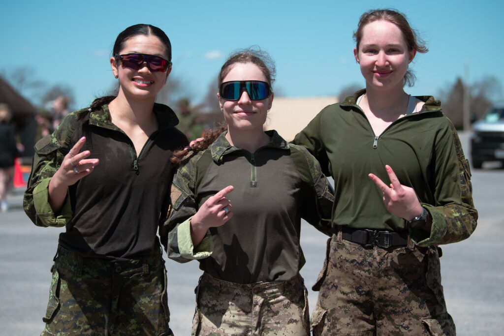 Three people in military camouflage uniforms standing outside and smiling for the camera.
