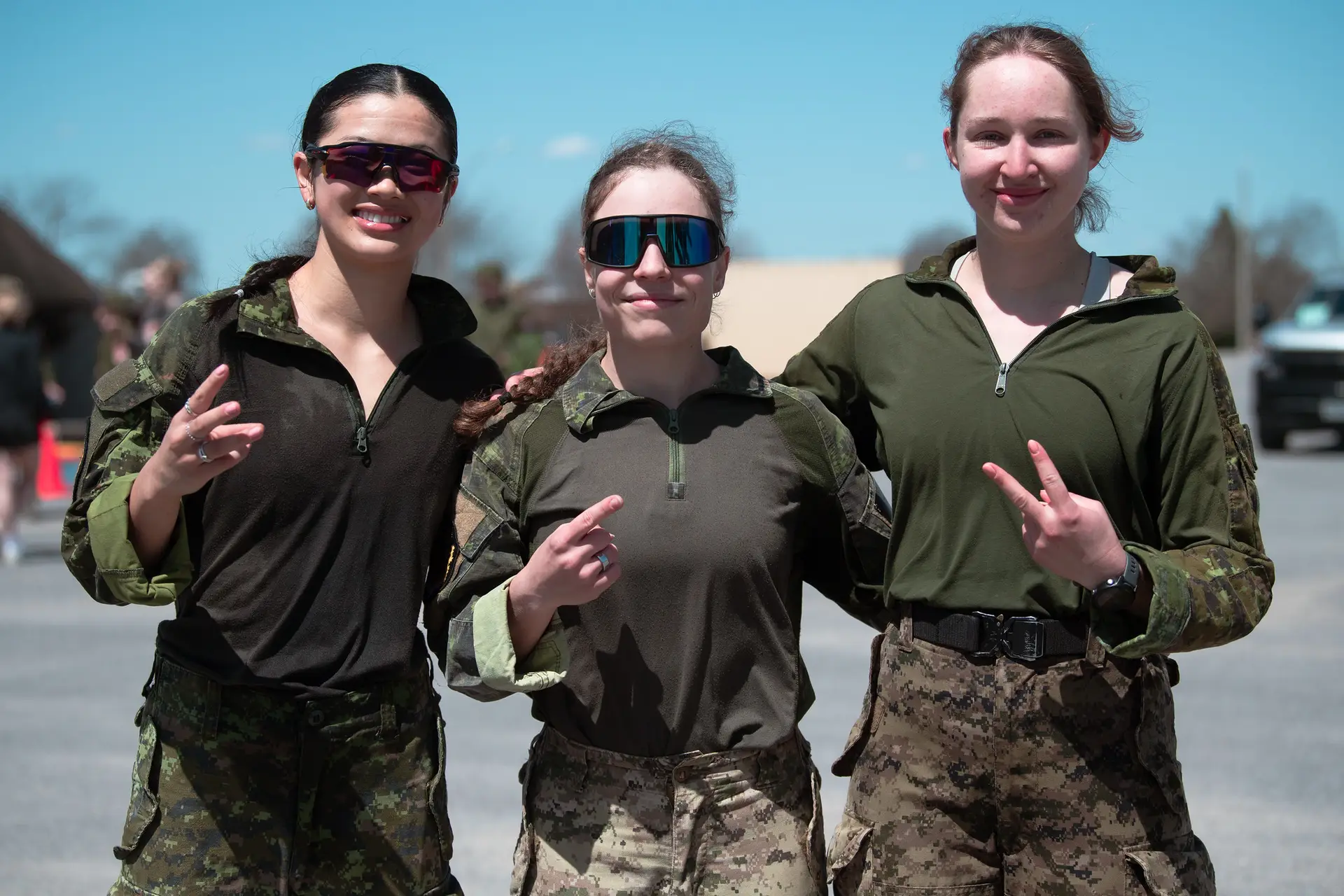 Three soldiers in military uniforms and sunglasses standing side-by-side, gesturing with their hands.