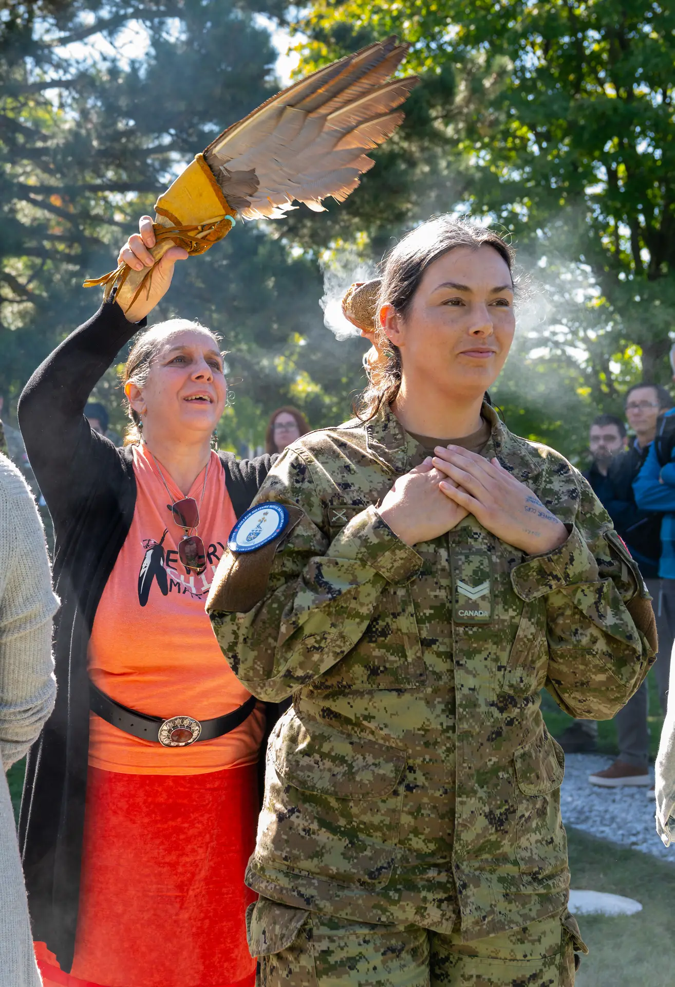 An Indigenous woman waves a feather fan to smudge a Canadian Armed Forces member who stands with hands over her heart.
