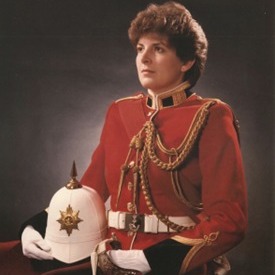 A person wearing a formal red military uniform with gold cord and a white belt, holding a white spiked helmet.