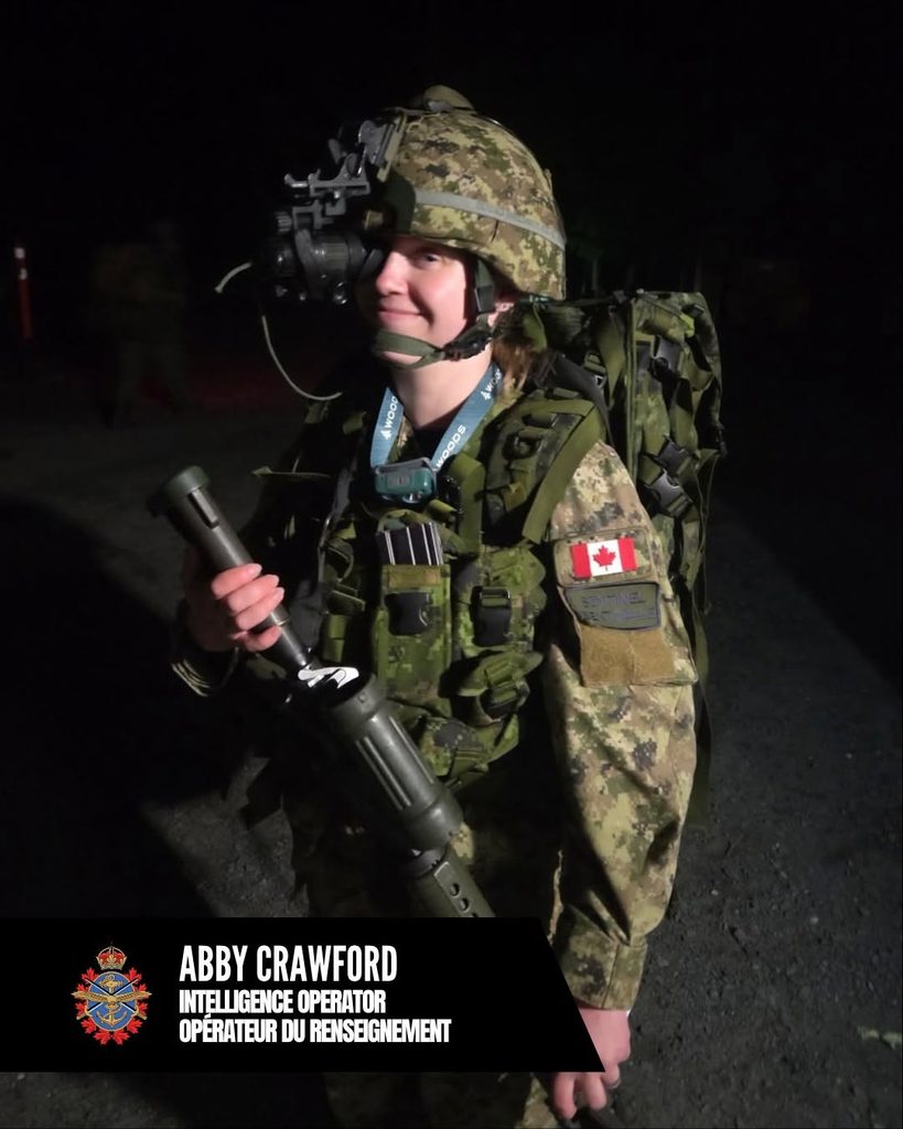 A Canadian Armed Forces Intelligence Operator in camouflage uniform and helmet with night-vision goggles holding a piece of tactical equipment, representing a member of the CAF Women’s Rugby community.