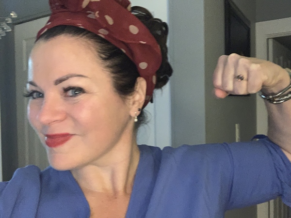 A woman wearing a red polka-dot headscarf and a blue top flexes her bicep in a Rosie the Riveter pose.
