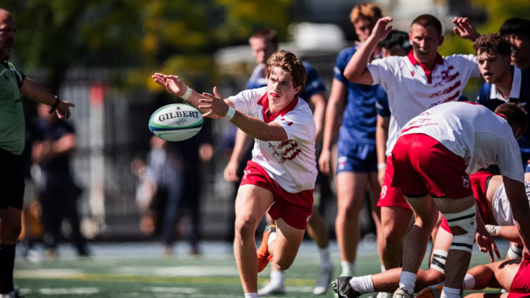 A rugby player in a white and red kit passes a Gilbert rugby ball during a match.