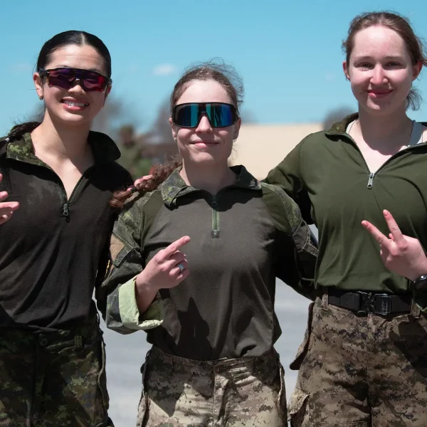 Three soldiers in military uniforms and sunglasses standing side-by-side, gesturing with their hands.
