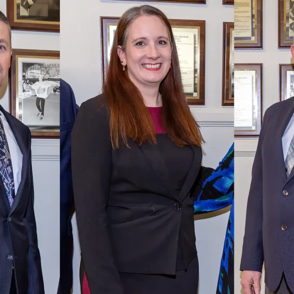 Three people in business attire stand indoors against a wall decorated with framed photos and documents, posing separately for formal portraits.